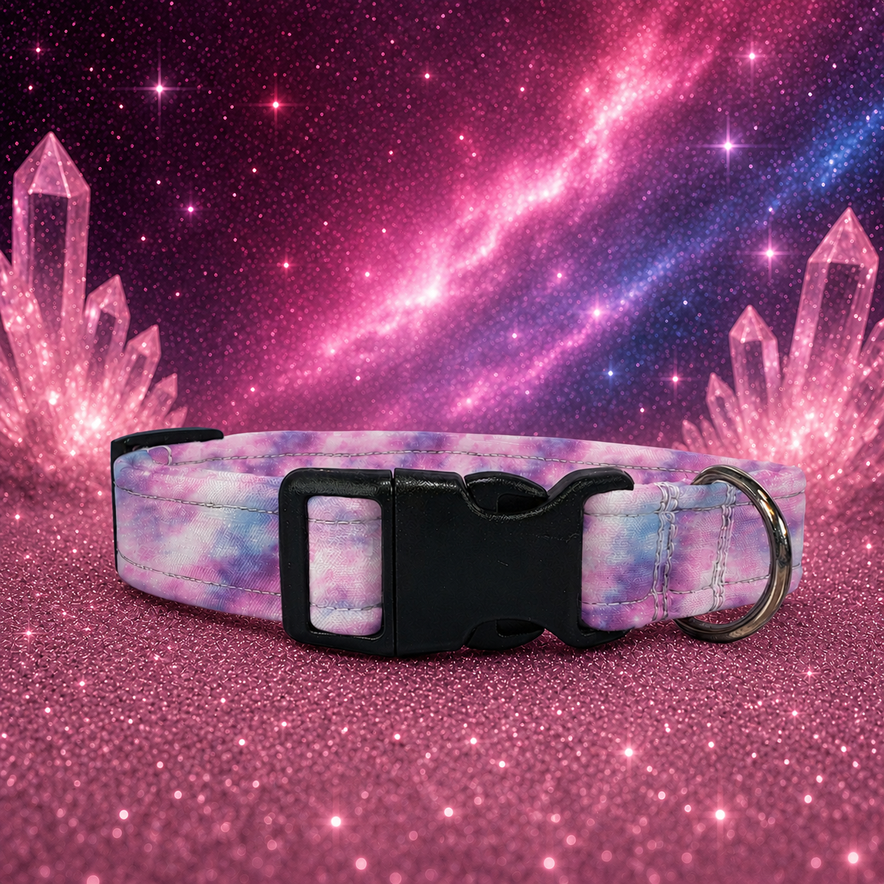 A pet collar with a pastel galaxy print in pink, purple, and blue, featuring a black plastic buckle and a silver metal ring, set against a glittery pink background with a cosmic galaxy design.